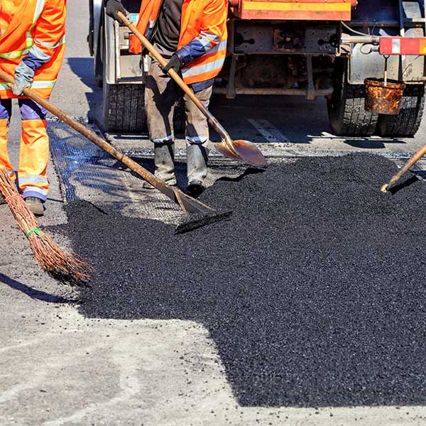 The working team smoothes hot asphalt with shovels